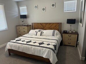 A bedroom with a wooden bed, two bedside tables, a nightstand, and a wall-mounted lamp.