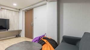 A modern living room with a grey sofa, a small table, and a television on a wooden panel wall. - K Space Inn Owen - Hostel (Singapore)