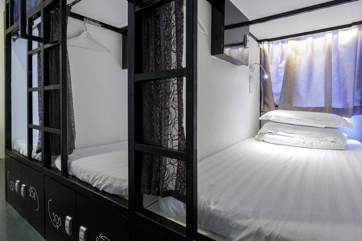 A bunk bed room with a window and curtains, a bedside table, and a wall-mounted light.