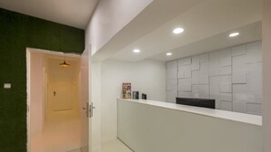 A reception area with a white reception desk, a green wall, and a tiled wall with a geometric pattern. - K Space Inn Owen - Hostel (Singapore)
