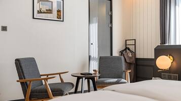 Habitación de hotel con una cama, dos sillones, una mesita, perchero y un cuadro en la pared.