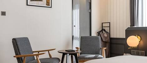 A hotel room with a bed, two armchairs, a small table, a coat rack, and a framed picture on the wall.