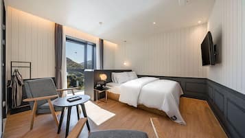 Habitación de hotel moderna con una cama grande, un escritorio, una silla, un televisor montado en la pared y vistas al exterior.