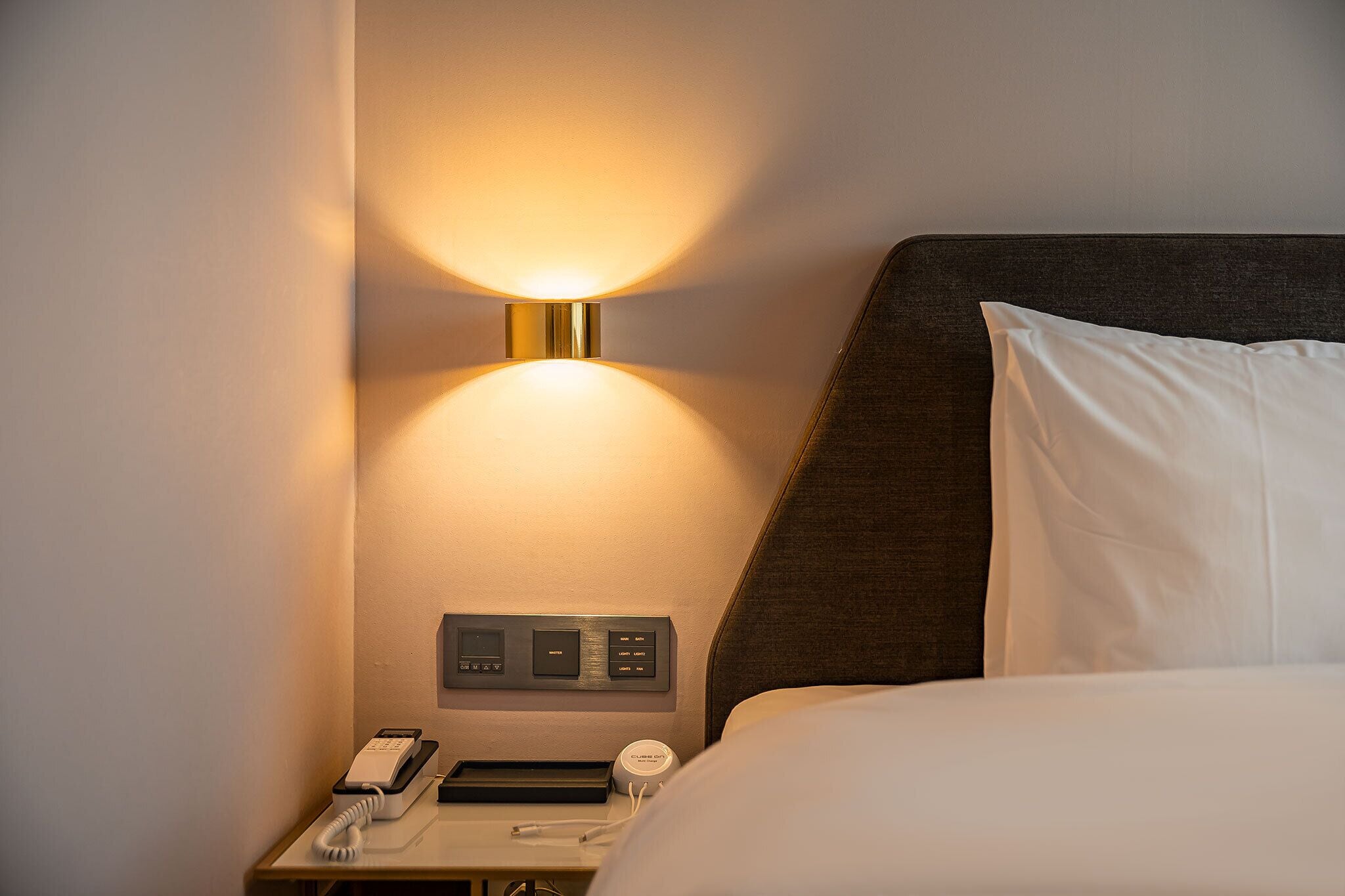Habitación de hotel con mesita de noche, lámpara, teléfono y panel de control.
