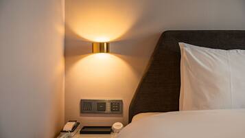 Habitación de hotel con mesita de noche, lámpara, teléfono y panel de control.