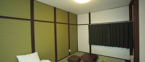 A hotel room with a bed, a small table, two stools, and a window with curtains.