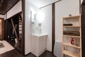 Un baño pequeño con un lavamanos blanco, espejo y estantes con toallas y una plancha.