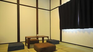 Um espaço com tatames, uma mesa de madeira baixa, dois almofadas e uma cortina preta.