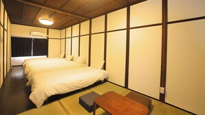 Quarto de hotel com duas camas, esteiras de tatame, um banco de madeira e uma luminária no teto.
