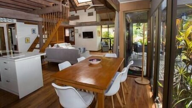A modern kitchen with a wooden table and white chairs, a staircase, and a view of the outdoors. - Stay at 'Banfield 4' (Wongaling Beach)