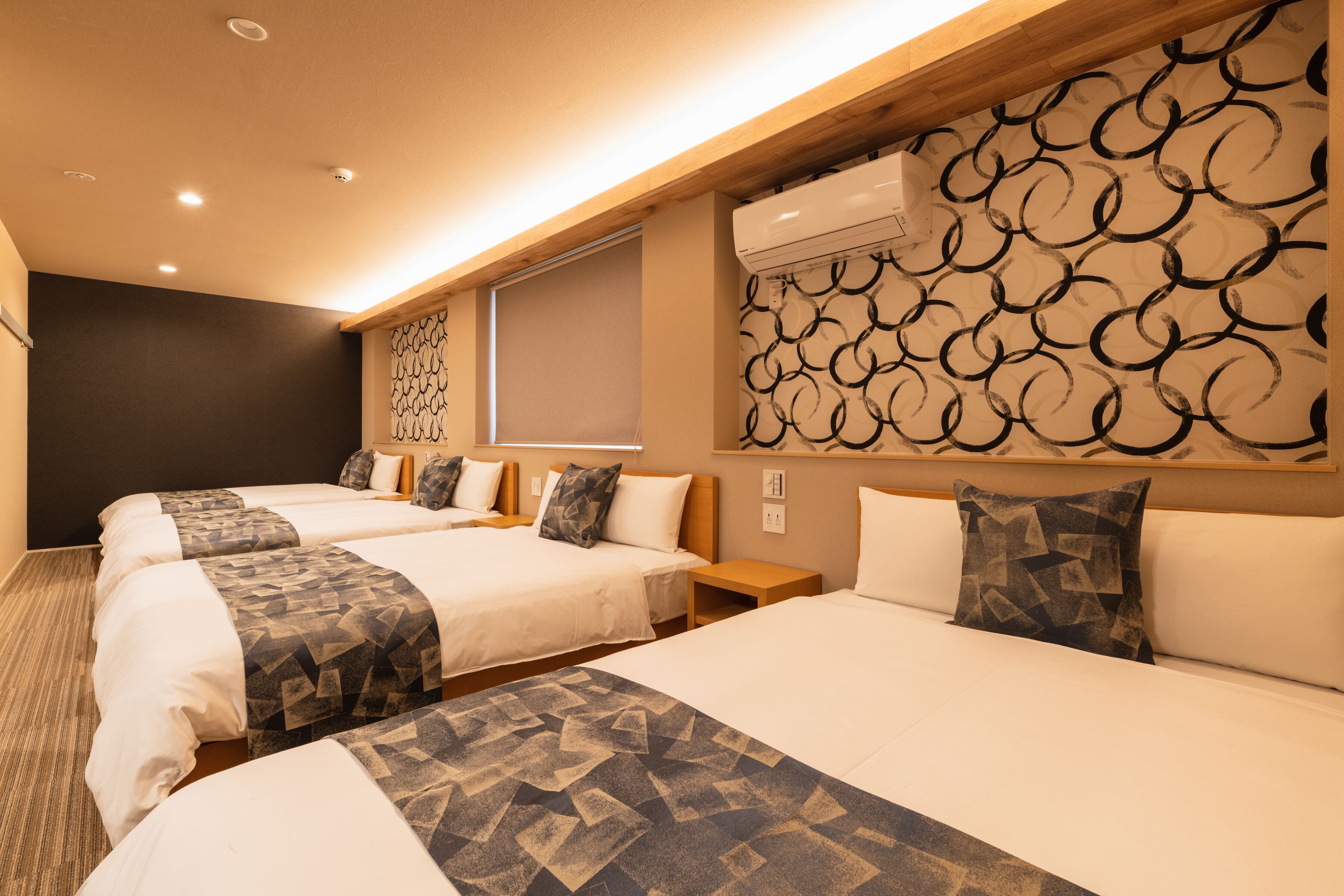 Habitación de hotel con cuatro camas, un ventanal con vistas y una pared con diseño.