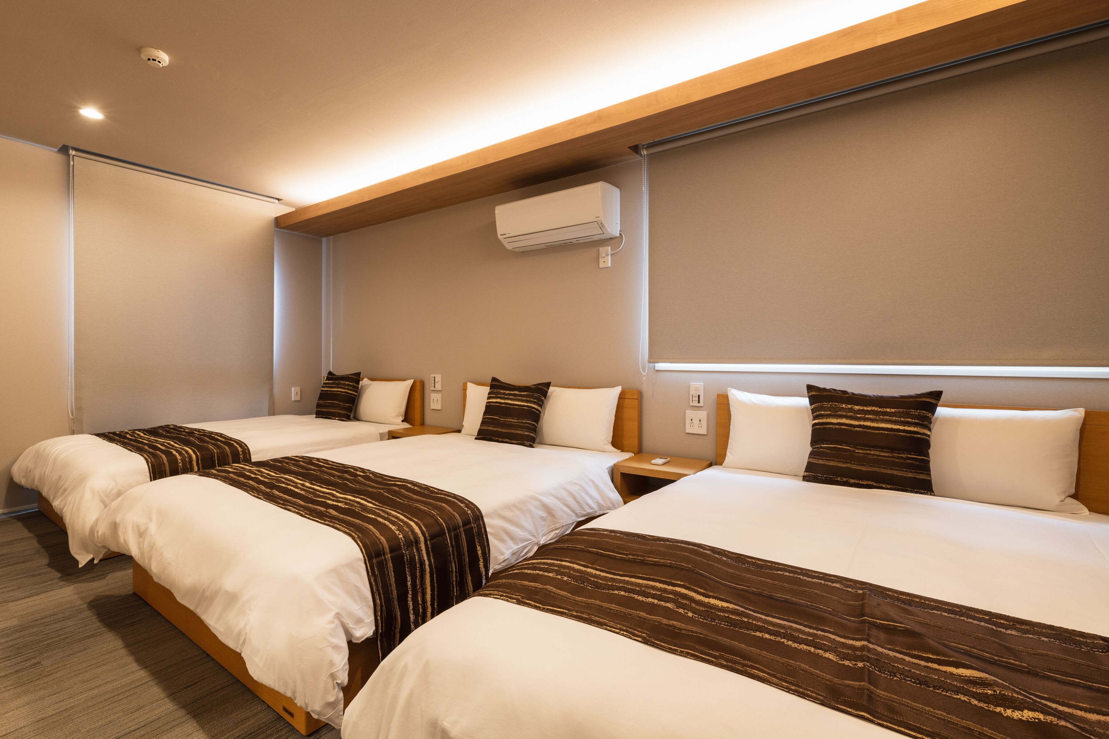 A hotel room with two beds, a ceiling air conditioner, and a window with a blind.