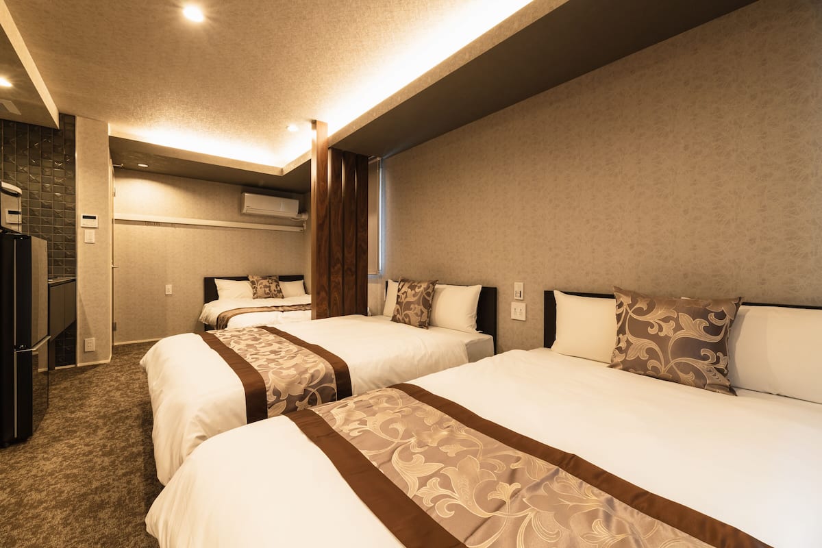 A hotel room with three beds, a kitchenette, and a bathroom.