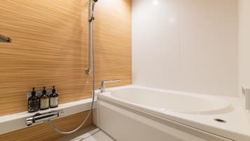 A modern bathroom with a wooden wall, a white bathtub, and a shower. There are bottles of shampoo and body soap on the wall.