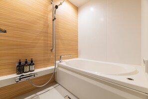 A modern bathroom with a wooden wall, a white bathtub, and a shower. There are bottles of shampoo and body soap on the wall.
