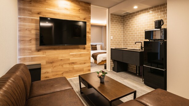 A modern living room with a flat-screen TV, a brown leather sofa, and a wooden accent wall. - Grand Base Urakami (Nagasaki)