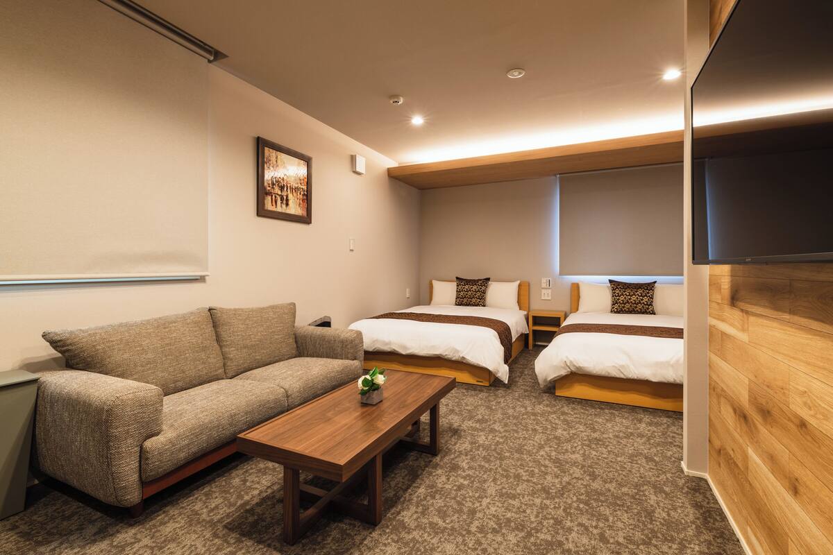 A hotel room with a sofa, two single beds, a wooden coffee table, and a picture on the wall.