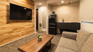A modern living room with a wooden wall, a flat-screen TV, a coffee table with a flower, and a sofa. - Grand Base Urakami (Nagasaki)