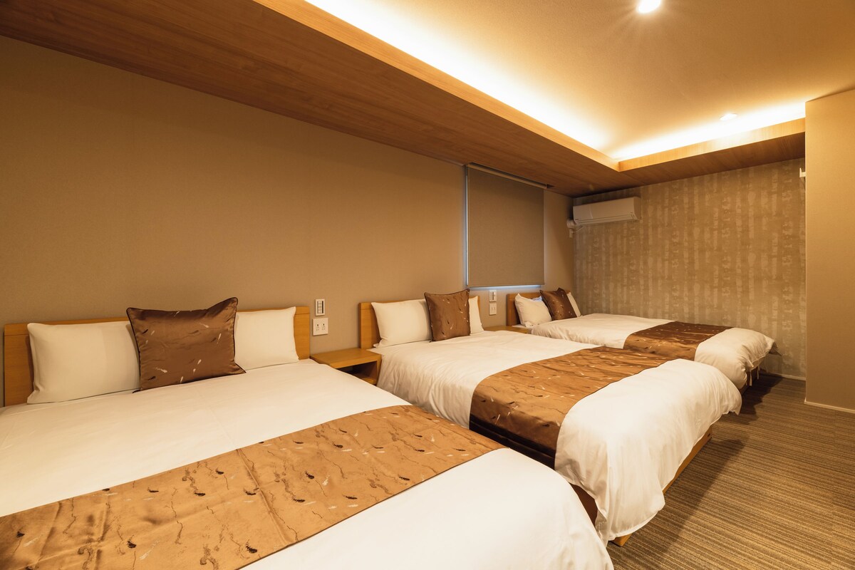 Une chambre d’hôtel avec trois lits, des têtes de lit en bois et un sol recouvert de moquette.