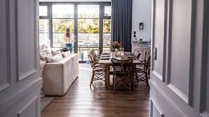 A modern interior with a wooden floor, a dining area with wicker chairs, and a large window overlooking a deck.