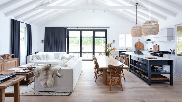 A spacious living area with a high ceiling, a dining table with chairs, a sofa, and a kitchen area with a large island.