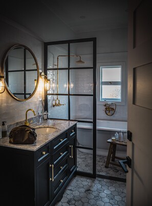 Un baño con lavamanos de mármol, muebles de color negro, un espejo redondo y una ventana con vistas.