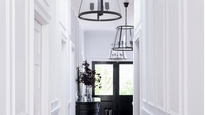 A hallway with white wainscoting, a black console table with a vase of flowers, and a black and white patterned rug.