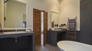 Un baño moderno con una bañera grande, dos lavamanos y una puerta de madera que da a otra habitación.