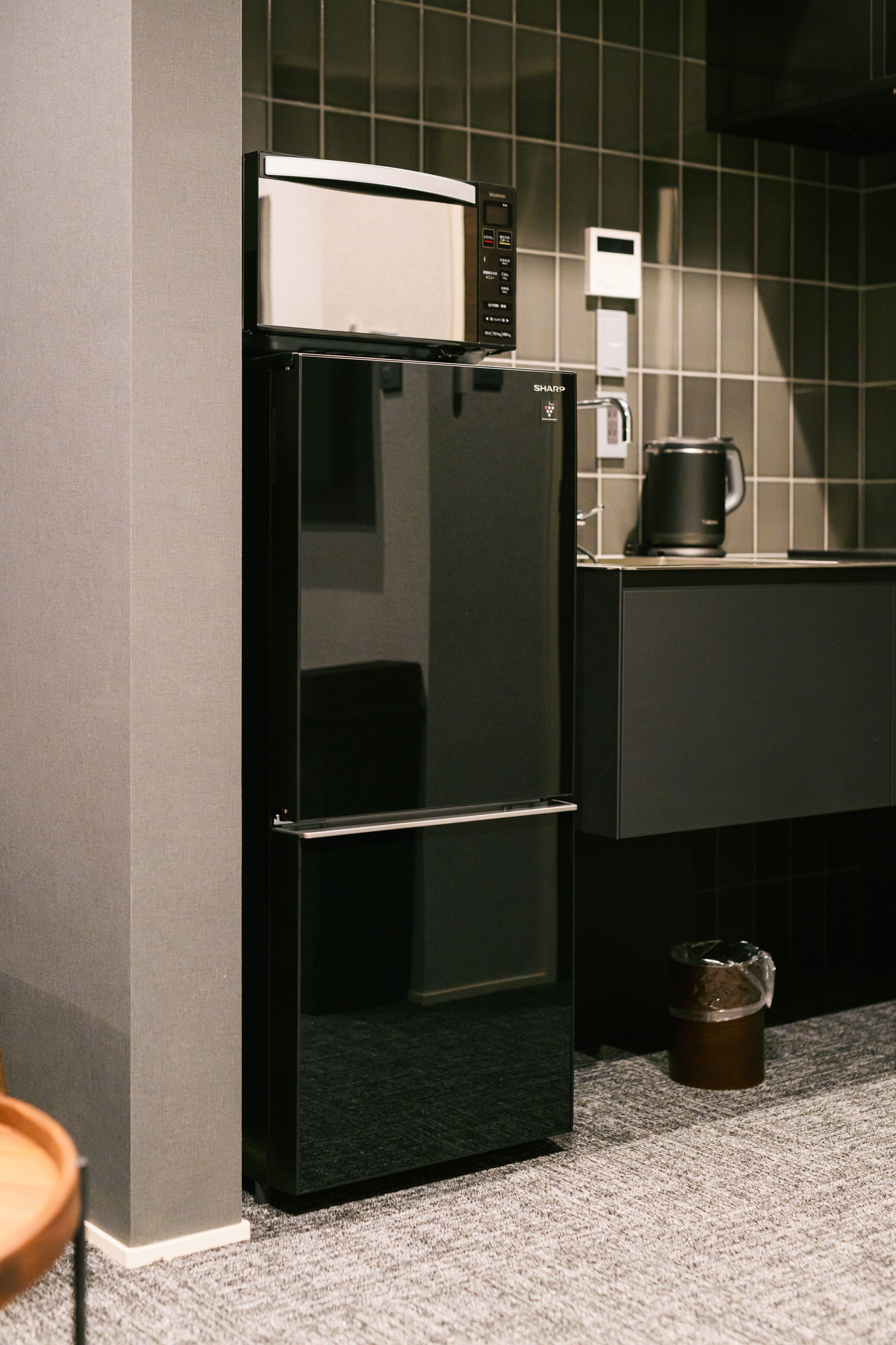 A kitchen with a black refrigerator, a coffee maker, and a trash bin.