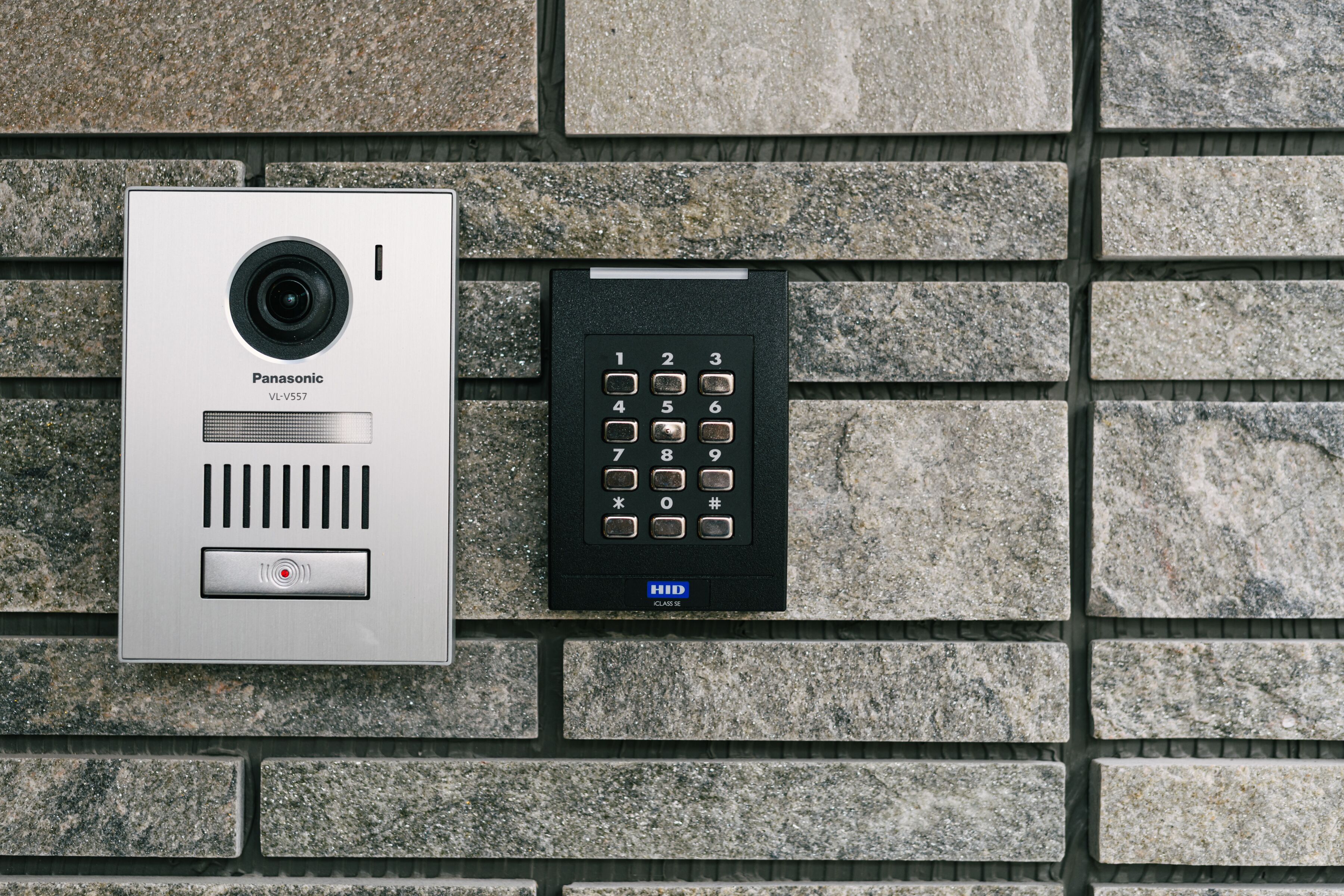 Un interphone Panasonic VL-V557 et un clavier de sécurité HID fixés sur un mur en pierre.