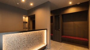 A modern reception area with a textured light-up wall, a bench, and a door leading to a seating area. - GRAND BASE Hakata Premium (Fukuoka)