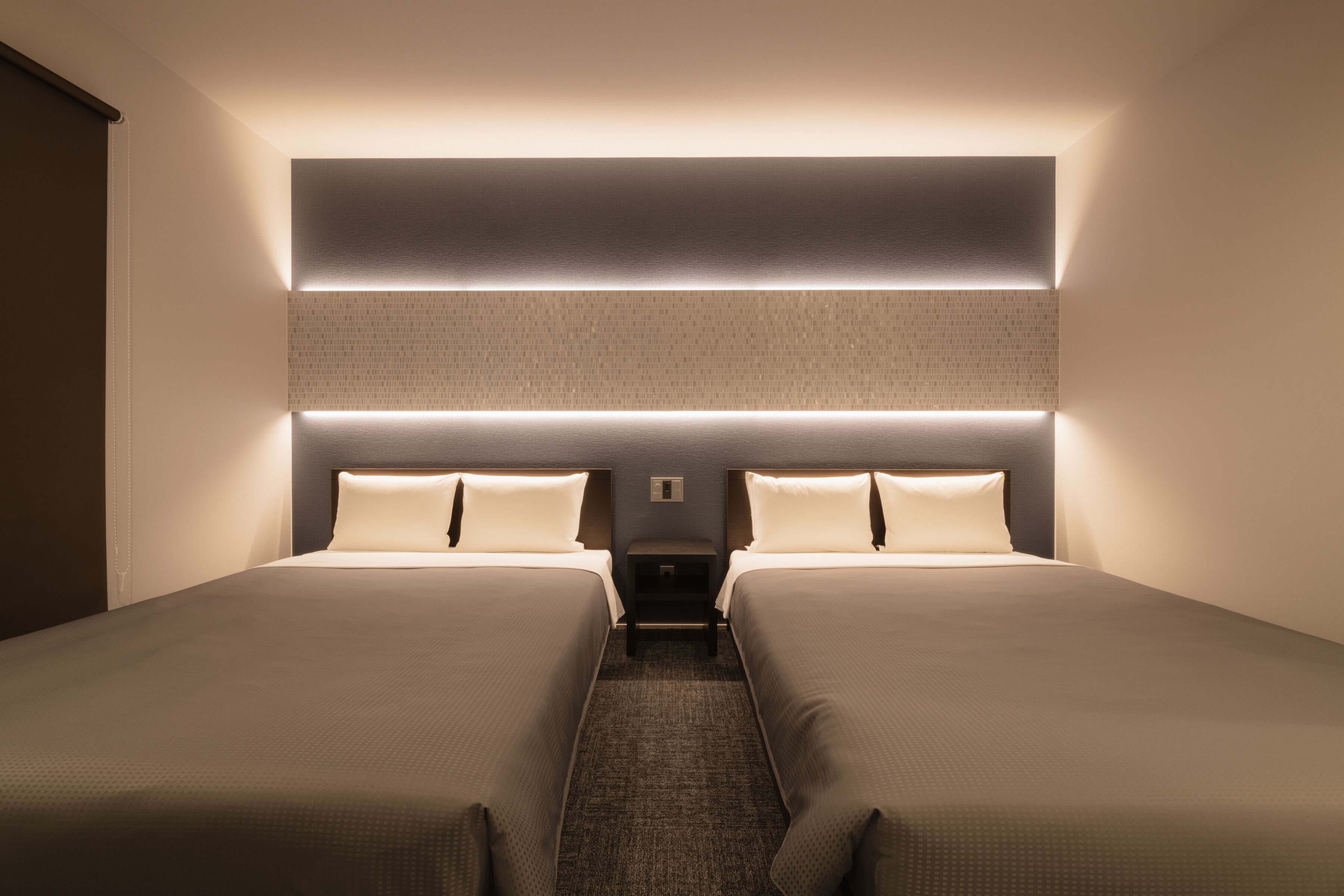 Una habitación de hotel con dos camas, una mesita de noche y una lámpara fijada a la pared.
