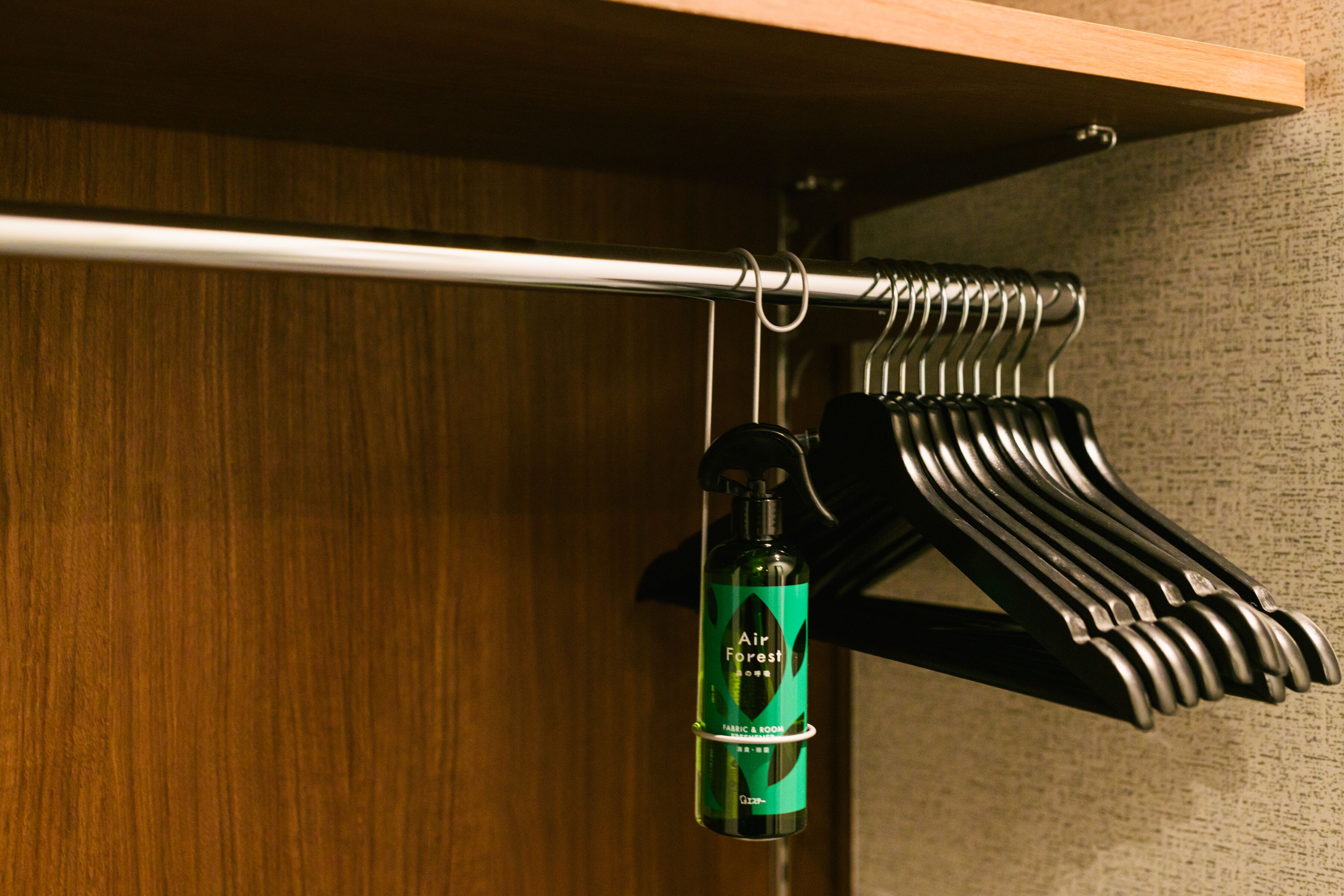 A wooden closet with a hanging rod and a bottle labeled "Air Forest" on a hook.