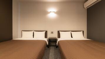 A hotel room with two beds, a nightstand, a wall-mounted light, and an air conditioning unit.