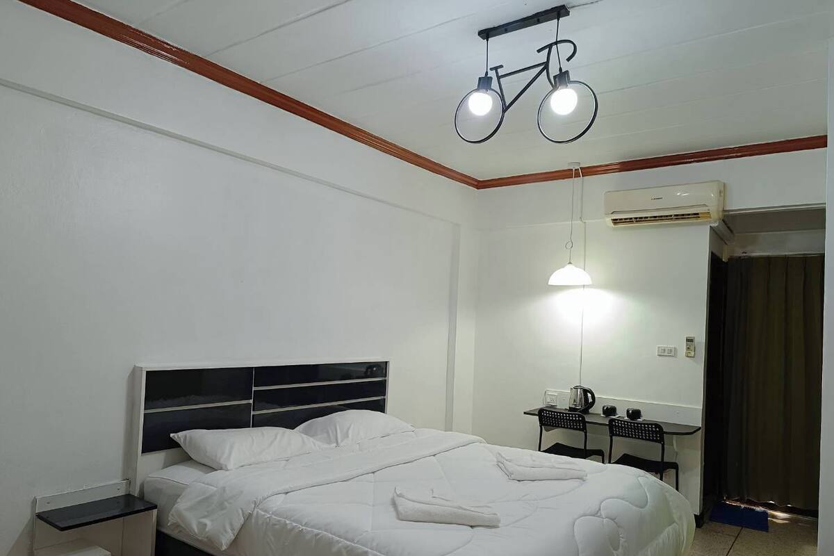 A hotel room with a bed, bedside table, lamp, and a desk with a chair.