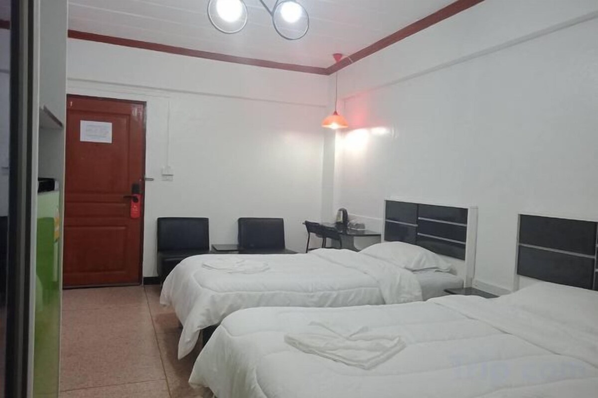 A hotel room with two beds, a desk, a chair, and a door.