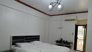A bedroom with a bed, bedside table, and a desk with a chair. There is an air conditioning unit on the wall and a door leading outside. - Hotel Paraiso (Bangkok)