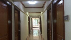 A long, narrow hallway with wooden doors on both sides, a tiled floor, and a ceiling with recessed lighting. - Hotel Paraiso (Bangkok)