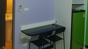 A compact kitchenette with a built-in air conditioner, a small table with two chairs, and a green refrigerator. - Hotel Paraiso (Bangkok)
