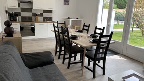 Eine moderne Küche mit weißen Schränken, ein Essbereich mit einem Holztisch und schwarzen Stühlen sowie ein großes Fenster mit Blick ins Freie.