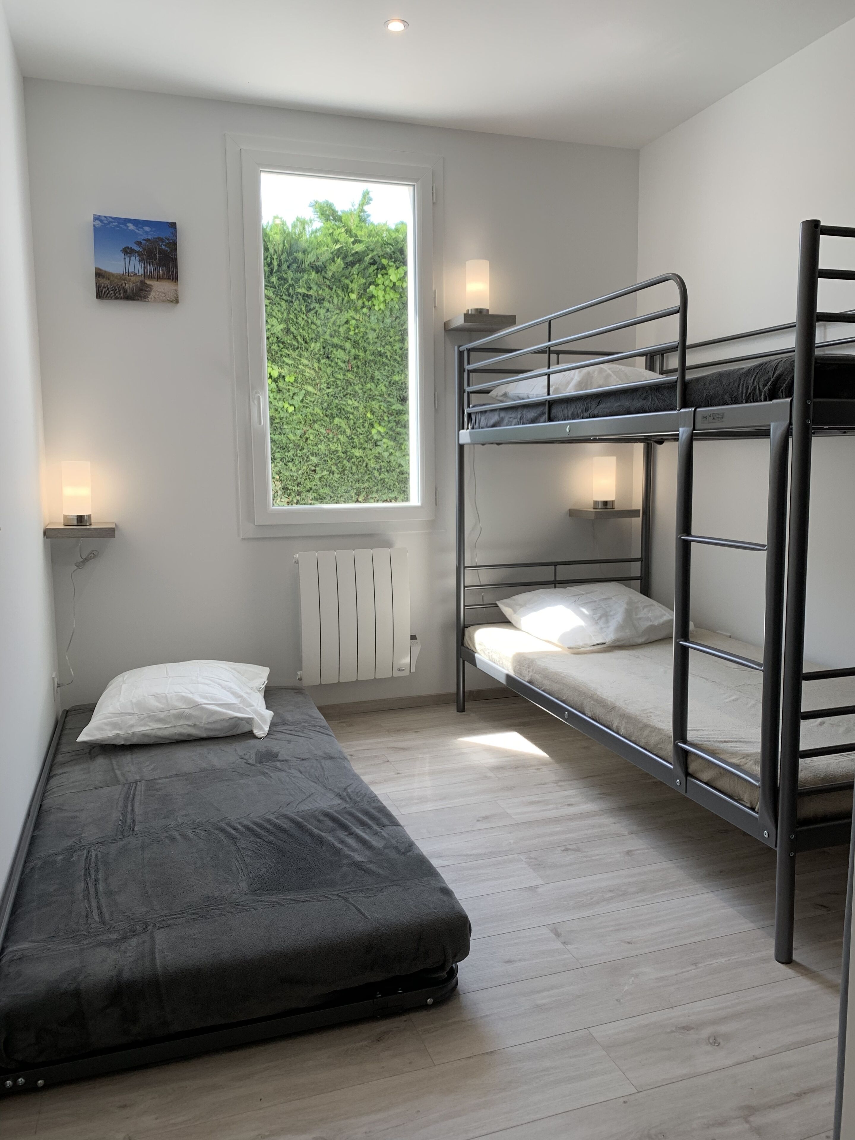 Une chambre de dortoir avec des lits superposés, un lit simple, une fenêtre donnant sur un espace verdoyant et une lampe fixée au mur.
