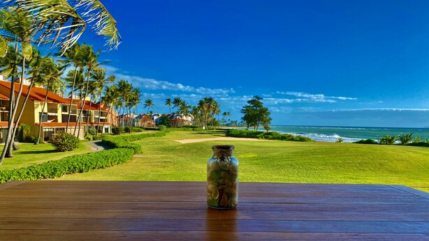 A wooden table with a glass jar in the center, overlooking a golf course and ocean view. - Gorgeous View- Beach Village at Palmas Del Mar (Palmas del Mar)