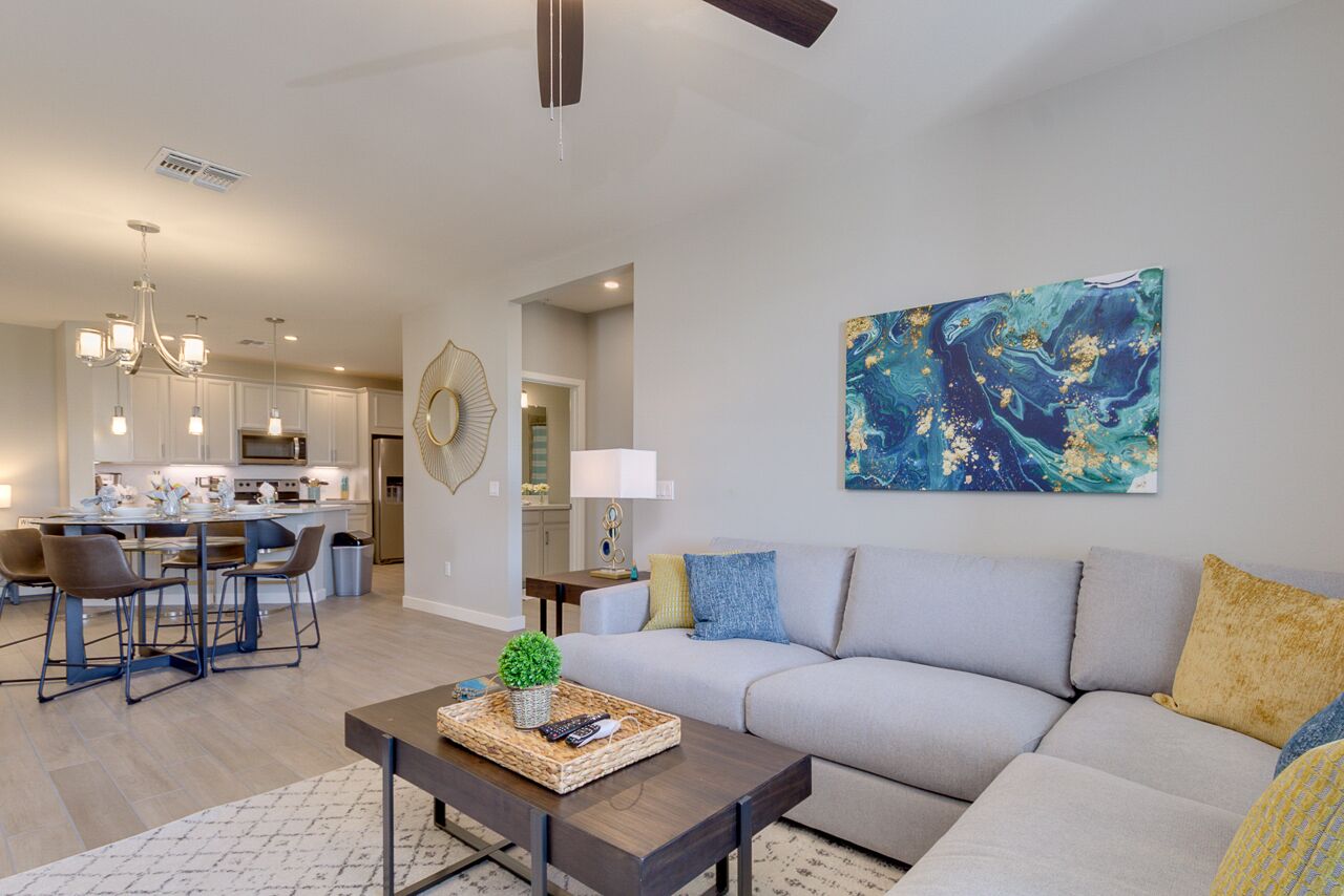 A modern living room with a sofa, coffee table, and dining area. There is a kitchen in the background with white cabinets and stainless steel appliances.