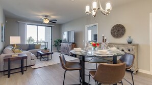 A modern living room with a sofa, coffee table, and dining table set for four. A ceiling fan and chandelier are visible. - Picture Perfect 2/2 with Views Galore! The Cays at Ocotillo! 30 Night Minimum Stay! (Chandler)