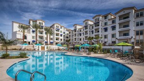 A swimming pool with lounge chairs and umbrellas, surrounded by multi-story buildings with balconies. - Picture Perfect 2/2 with Views Galore! The Cays at Ocotillo! 30 Night Minimum Stay! (Chandler)