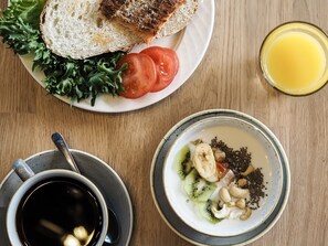 A breakfast setting with toast, tomatoes, greens, a bowl of fruit and seeds, a cup of coffee, and a glass of orange juice. - Hotel Fabrik Forssa (Forssa)