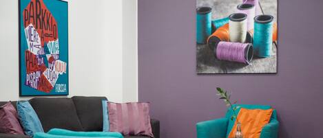 A modern living room with teal and gray sofas, a round coffee table, and a purple accent wall.