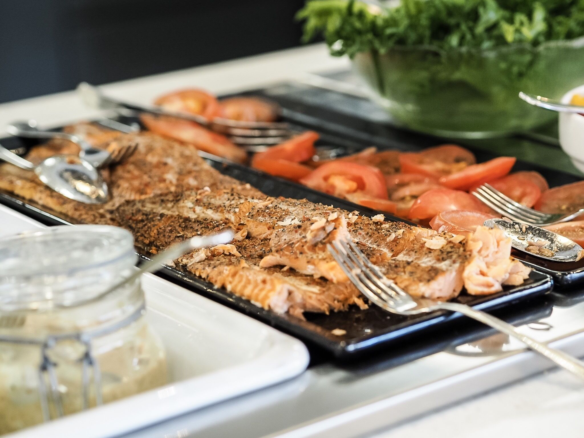 Un buffet proposant du poisson grillé, des tomates en tranches et un grand saladier de salade.