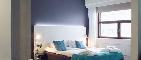 Quarto moderno com uma cama grande, mesas de cabeceira, uma escrivaninha e uma janela que proporciona luz natural.