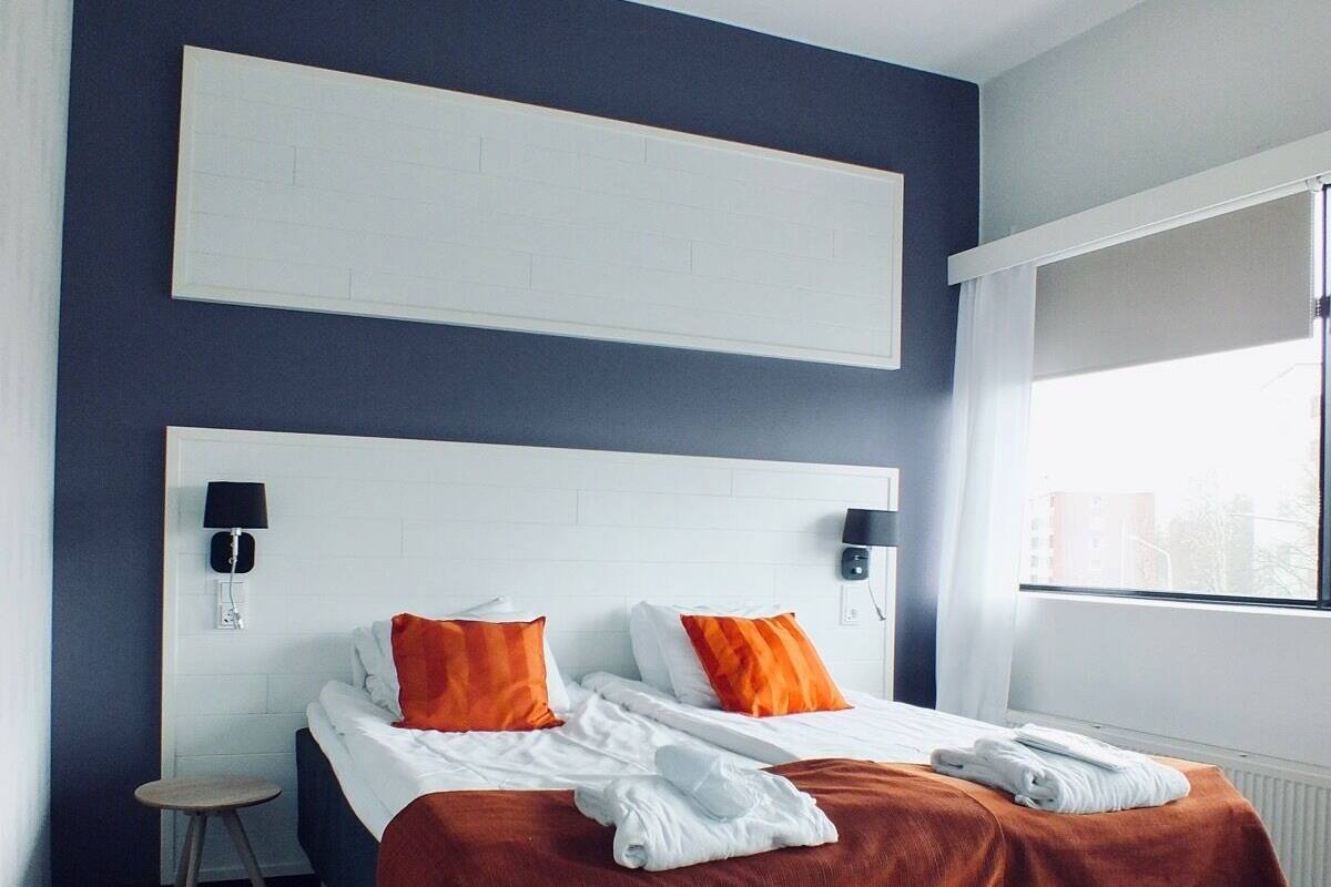Moderni hotellihuone, jossa on suuri sänky, kaksi tyynyä, pieni yöpöytä ja ikkuna, josta on näkymä.